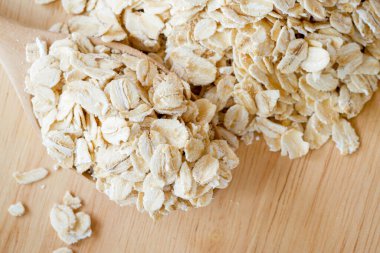 Ahşap zemini olan bir yulaf yığınının üzerinde ahşap bir kaşıkta yuvarlanmış yulaf. Sağlıklı gıda konsepti, üst görünüm.