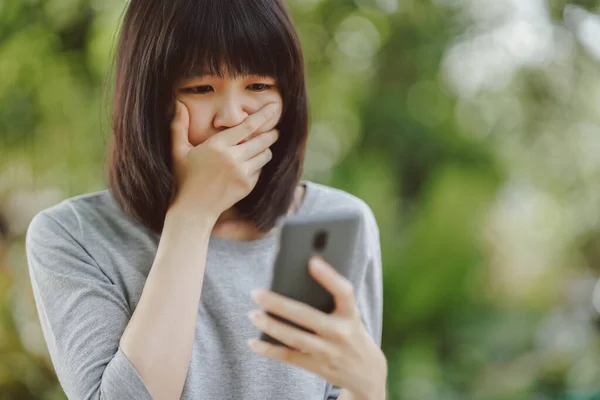 Woman using smartphone with shocked and sad face with blurred nature background.