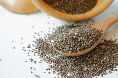 Chia tohumları bir masaya yığıldı ve beyaz bir arka planda tahta bir kaşıkta.