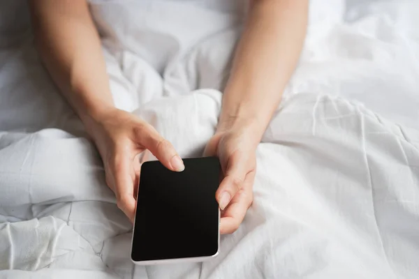 Woman\'s hand holding phone with black blank screen on bed. Clipping path.