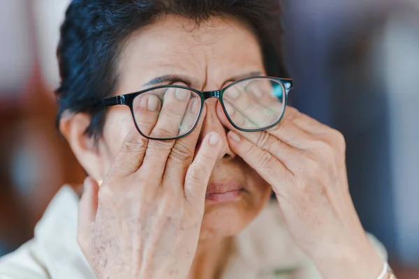 An elderly woman uses her hand to massage her eyes due to fatigue. and have blurred vision. Concept of health problems in the elderly.