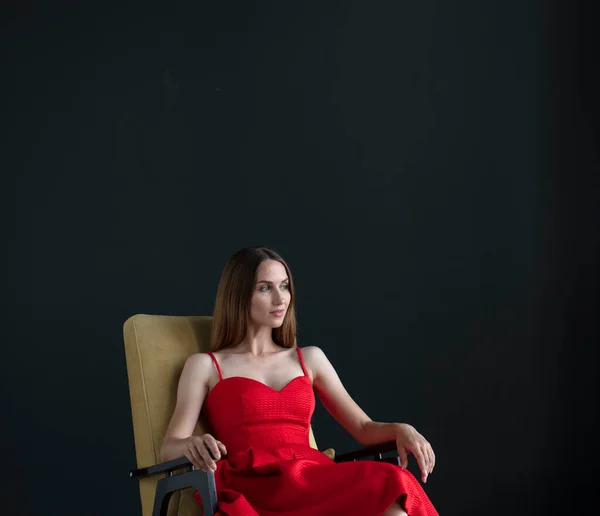 Portret Pięknej Młodej Kobiety Siedzącej Krześle Czerwonej Sukience Ciemnym Tle — Zdjęcie stockowe