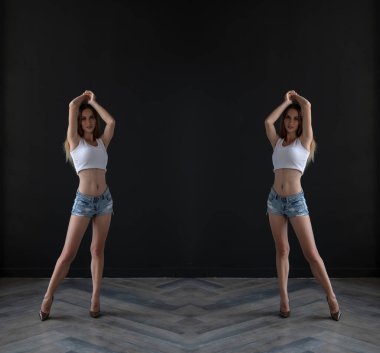 mirrored shot of slim blonde young woman wearing top and shorts posing on dark background