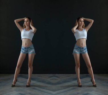 mirrored shot of slim blonde young woman wearing top and shorts posing on dark background