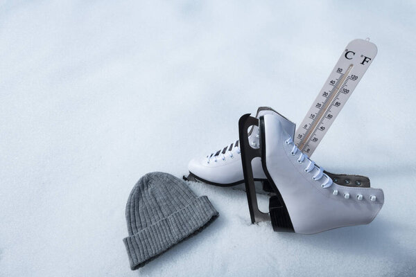 Пара белых коньков рядом с серой шерстяной шапкой и термометром, размещенными на естественном снегу