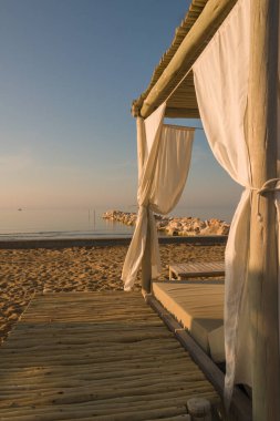 Sahilde beyaz çarşaflarla kaplı romantik bir şezlong.