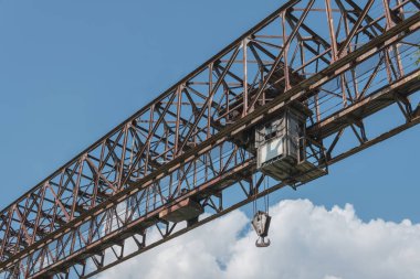 Mavi gökyüzüne karşı büyük kancalı ve santral kulübesi olan paslı ağır vasıta vinç.