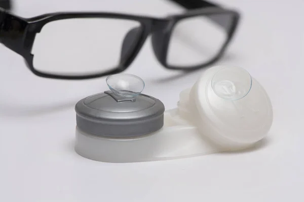 Beyaz arkaplanda izole edilmiş siyah optik gözlüklerin önündeki lens kutusundaki kontak lensler