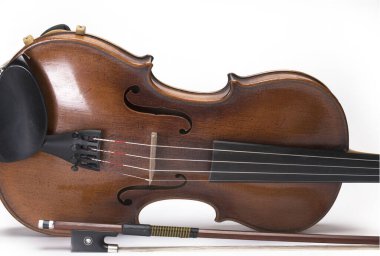 Close up of bow in front of sound body and strings of old violin with sound holes on white background