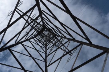 Büyük, yüksek voltajlı direğin ortasında yukarı bakan parçalı bulutlu mavi gökyüzüne karşı güç pilonları güç kaynağı ve elektrik kaynağı konsepti olarak.