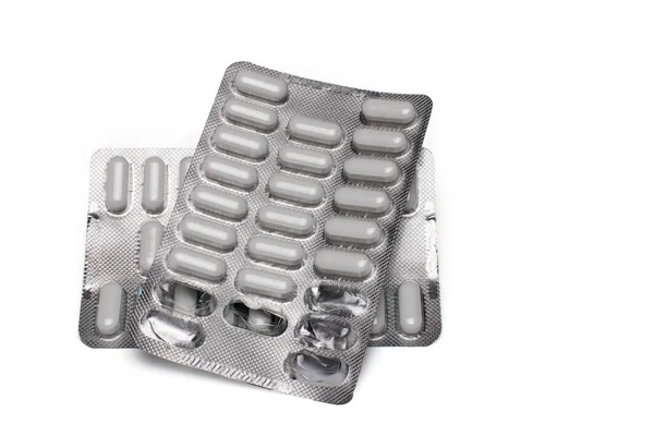 Birbirinin üzerine yığılmış iki gümüş metal, parlak hap şişkinliği, içinde beyaz haplar ve beyaz arka planda kayıp masalar var.