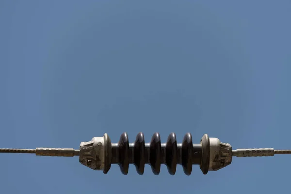 Close-up of an electric current insulator between two thick metal steel cables against a blue sky as a concept for line problems communication connection problems as well as dangers of electric energy