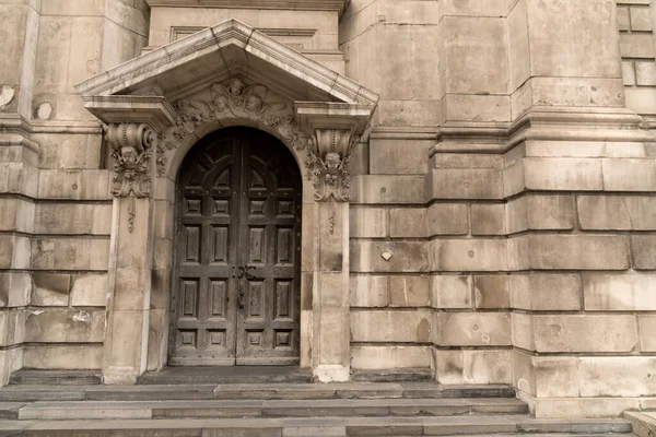 Detail of an entrance to a historic building with pointed canopy and geometrically rectangular facade and semicircular solid wooden door as a concept for antique architecture