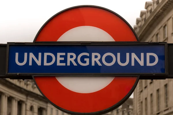 editorial close up of red blue underground metro subway sign in front of historic buildings and cloudy white sky in city of London as concept for public transport in UK