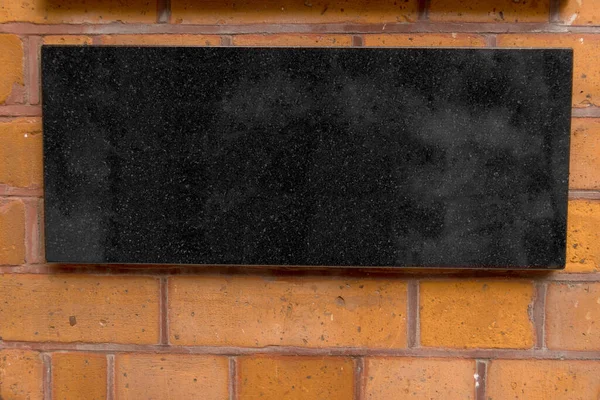 Close up of bricked wall facade laid of glazed fired bricks mounted black marble sign plate offering copy space to use as background