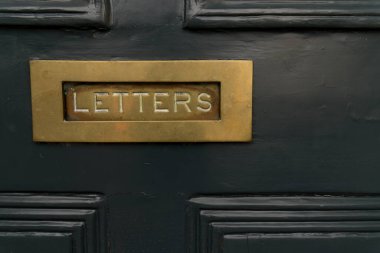 Close up of dark black noble wood entrance door with square mail slot with copper metal brass inscription Letters concept for mailings messages and letter delivery