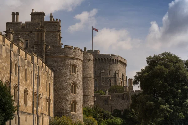 Windsor kalesi kısmi manzaralı önplanda yaldızlı çitler ve parçalı bulutlu mavi gökyüzüne karşı ağaçlar