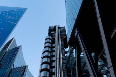 Aşağıdan mavi gökyüzüne karşı görünen modern gökdelenlerin altında iş bölgesi ve şehir merkezi konsepti olarak yapılandırılmış metal cam cepheler var.
