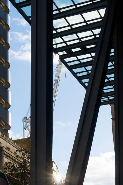 Looking up between massive steel beams at a tower crane at the construction site of a skyscraper in downtown against blue sky