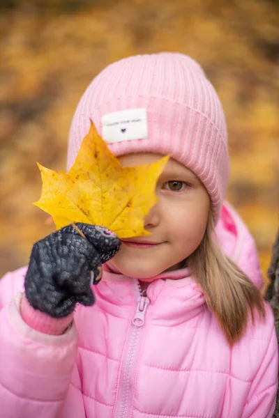 Ein Mädchen hält ein großes gelbes Ahornblatt in der Hand. — Stockfoto