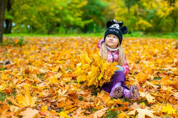 En flicka sitter bland ett stort antal gula lönnlöv — Stockfoto