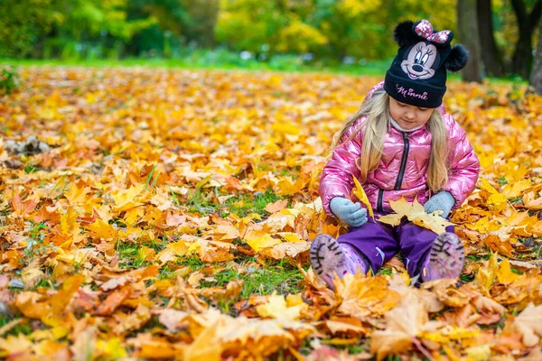 En flicka sitter bland ett stort antal gula lönnlöv — Stockfoto