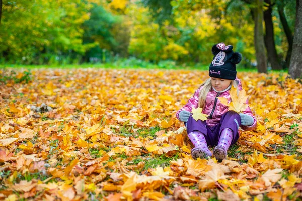 Bir kız çok sayıda sarı akçaağaç yapraklarının arasında oturuyor. — Stok fotoğraf