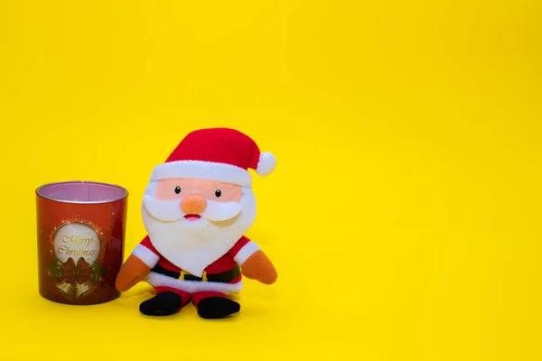 Stuffed funny Santa Claus and a glass candle on yellow background — Stock Photo, Image