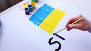 Bir kadın Ukrayna bayrağıyla bir poster çiziyor ve İngilizce 
