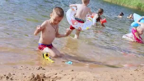 Menino feliz brincando com brinquedos de praia no lago ensolarado dia de verão, Marupe, Letônia - 07 Julho 2021 — Vídeo de Stock