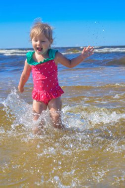 Avrupa görünümlü bir kız sahilde suda eğleniyor ve su sıçratıyor.