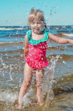 Avrupa görünümlü bir kız sahilde suda eğleniyor ve su sıçratıyor.