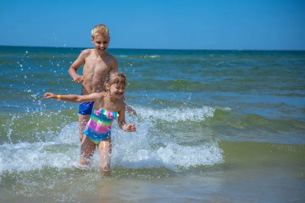 Дівчина і хлопчик розважаються у воді на пляжі і розбризкують Стокове Фото