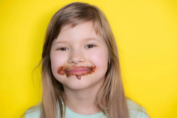 Happy and laughing little girl eating chocolate dirty face. Close up of kid with dirty face in chocolate or nutella.