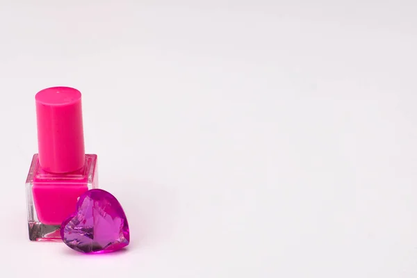 Pink nail polish with glass hearts of violet color on white background.Copy space. High quality photo