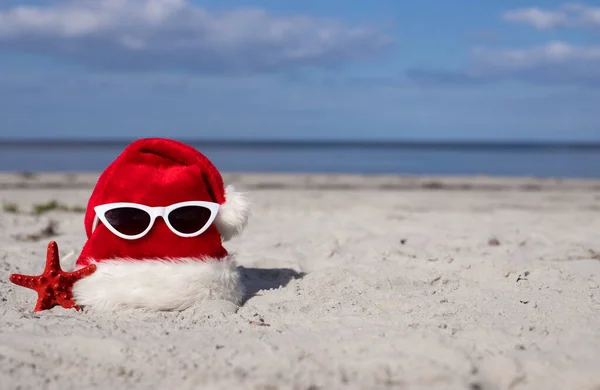 Christmas background Santa Claus hat on the beach with starfish and sunglases.Christmas card and advent calendar concept. Travel ticket sale concept for christmas holidays.Copy space.High quality