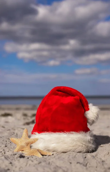 圣诞背景圣诞老人的帽子和海星在沙滩上 圣诞贺卡和日历的概念 圣诞假期的旅游票销售概念复制空间垂直摄影高质量的 — 图库照片