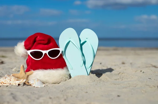 Christmas background Santa Claus hat on the beach with starfish,sunglases and beach slippers.Christmas card and advent calendar concept. Travel ticket sale concept for christmas holidays.Copy space