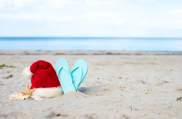 Christmas vacation at sea. Christmas background. Santa hat and beach sleepers on sandy beach.Christmas card and advent calendar concept. Travel ticket sale concept for christmas holidays.Copy space