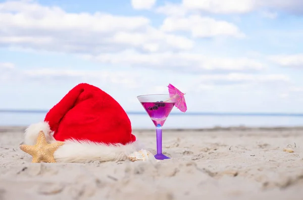 Christmas vacation at sea. Santa hat, starfish, coctail on sandy beach.Christmas card and advent calendar concept. Travel ticket sale concept for christmas holidays.Copy space.Close up.High quality