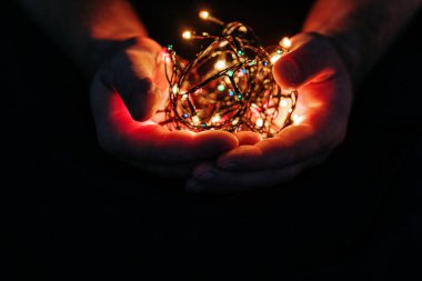 Erkek elleri, arka planda ışıkları olan ve metin için fotokopi alanı olan bir Noel çelengi tutuyor. Retro etki, yakın çekim. Kış, kartpostal şablonu