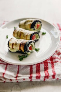 hafif bir arka plan üzerinde beyaz bir tabak üzerinde kızarmış patlıcan, süzme peynir ve domates geleneksel çanak üç rulo. Minimalizm. Yukarıdan görüntüle