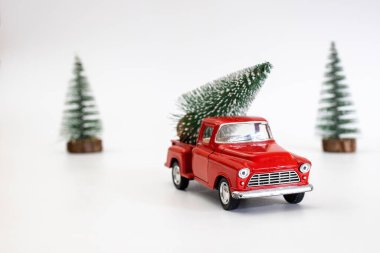 Arkadaki minyatür kırmızı araba beyaz izole bir arka planda bir Noel ağacı taşıyor. Yer ayırın. Kavram, şenlikli Noel havası, hediye teslimatı. Eğilim