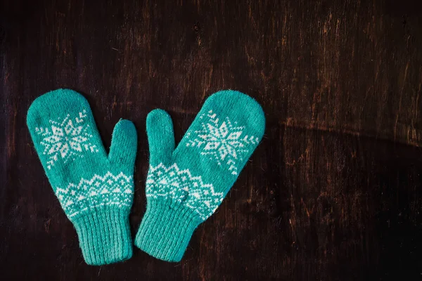 Koyu mavi-yeşil-kahverengi ahşap bir arka planda bir çift mavi örgü eldiven, boşluğu kopyala.