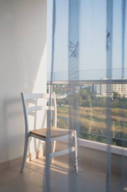 Denize bakan açık minimalist bir balkonda boş bir sandalye var.
