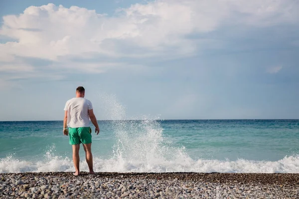 attractive young adult man stands with his back on the shore of the mediterranean sea with waves. copy space.