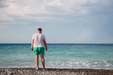 attractive young adult man stands with his back on the shore of the mediterranean sea with waves. copy space.