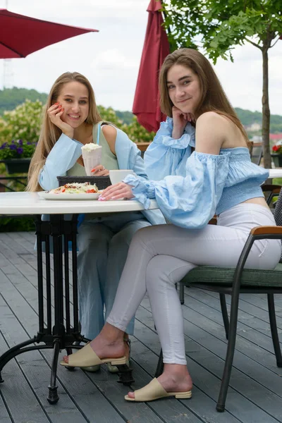 2人の若い女性の友人がカフェで朝食を取りニュースを話し笑っていました。カフェの女性はカクテルを飲み. — ストック写真
