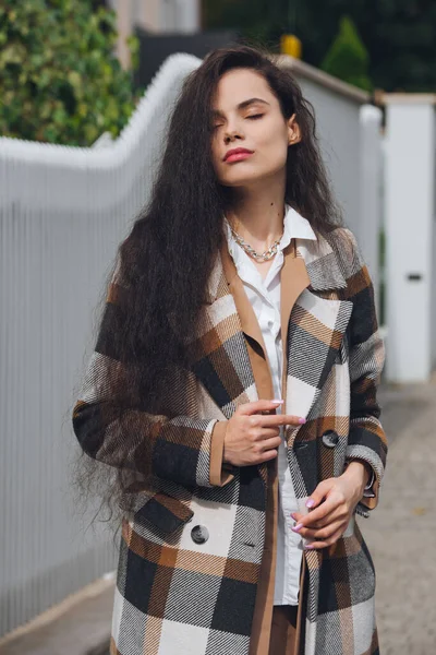 Portrait rapproché de jeune belle femme à la mode portant un long manteau à carreaux, un pantalon beige et une blouse blanche. Dame posant sur la rue de la ville. — Photo