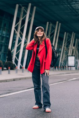 Modaya uygun giyinmiş, şehir geçmişine karşı poz veren çekici bir kadın. Tarz sahibi genç bir kadının açık hava moda portresi.